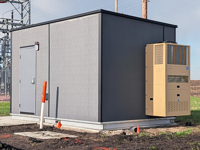 10ft-by-16ft-shelter-installed-2 Prefabricated utility control building at an electrical substation featuring a secure steel entry door and integrated HVAC system, providing reliable, climate-controlled protection for critical power, communications, and automation equipment.
